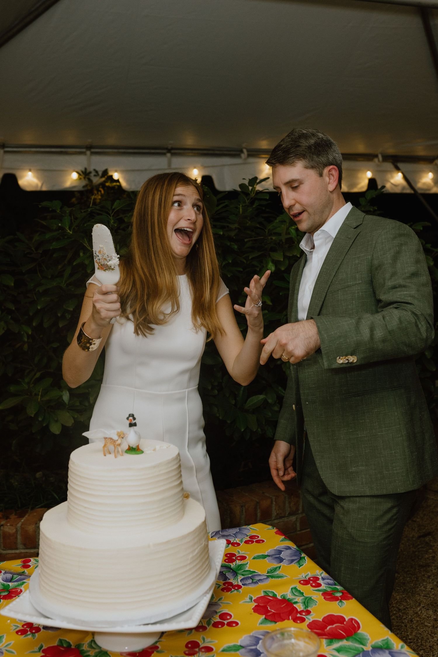 Couple sharing a joyful moment while cutting their white wedding cake.