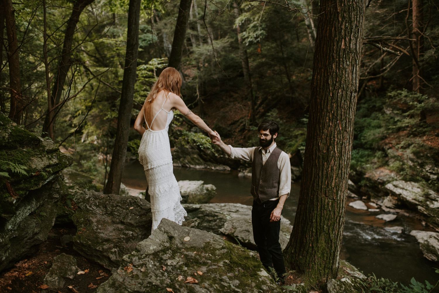 Two people share a romantic moment on a forest trail beside a creek.