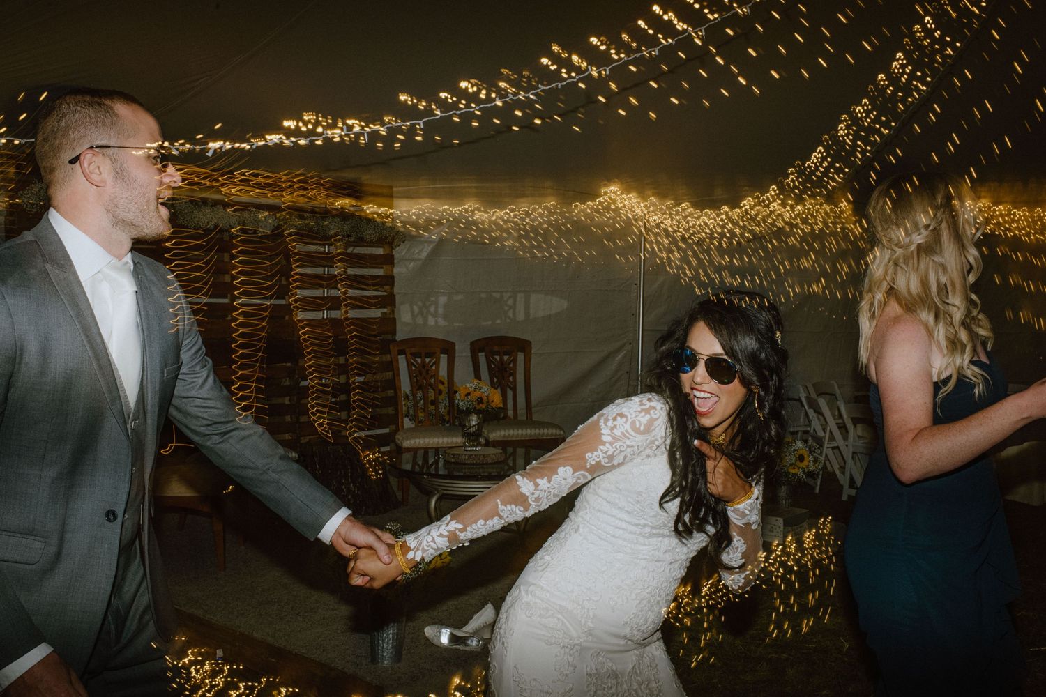 Couple dancing at a reception under twinkling string lights in a rustic venue.