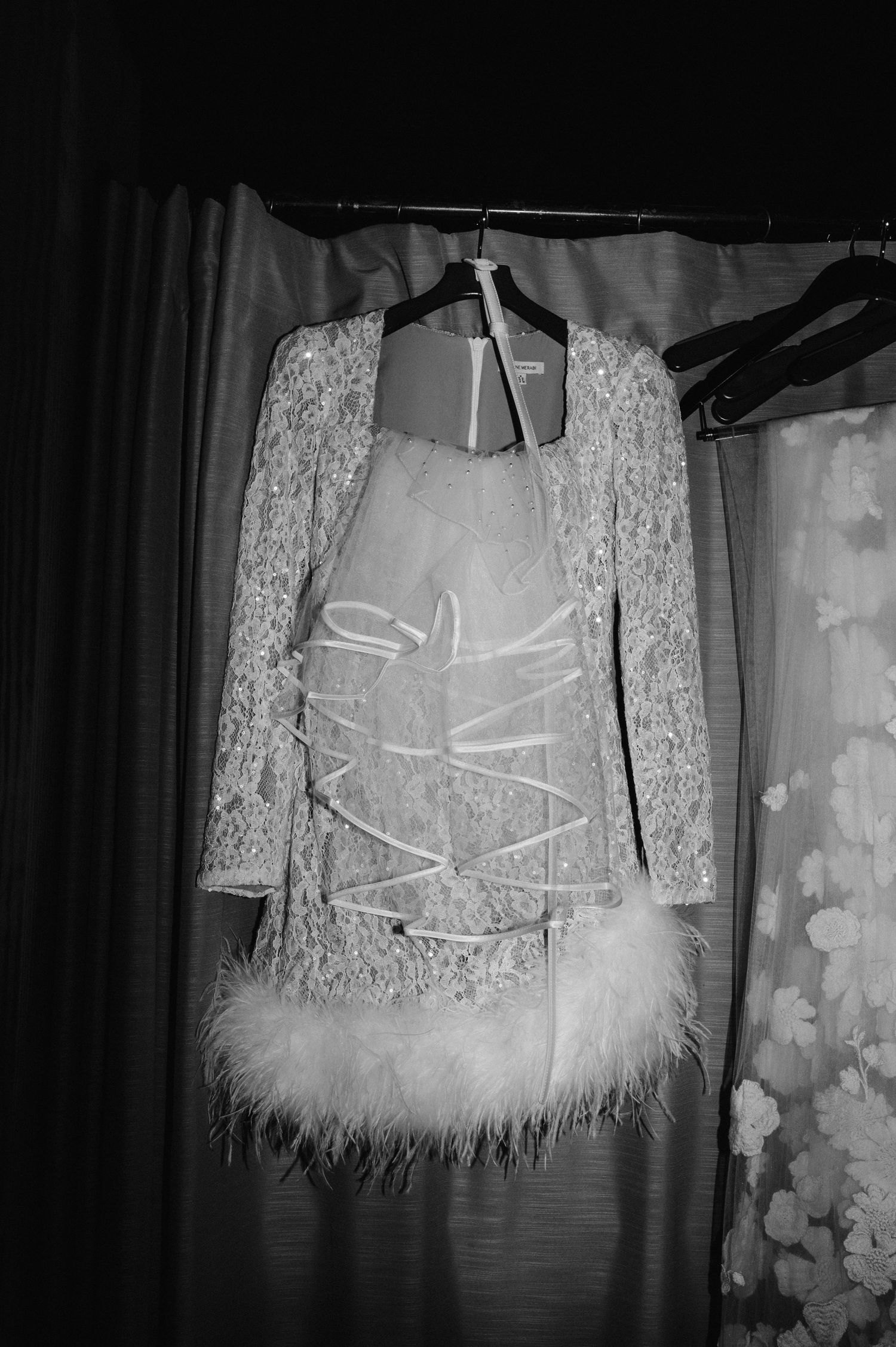 A white lace wedding dress with feather trim hanging on display.