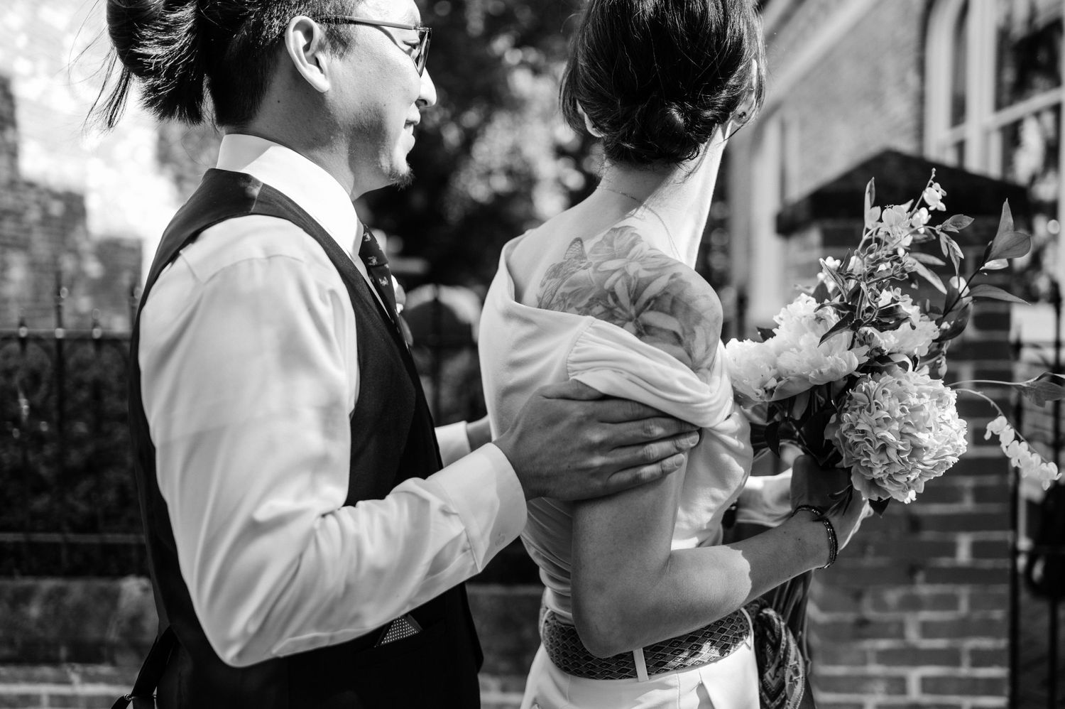 A black and white photo captures an intimate moment between newlyweds with a bouquet.