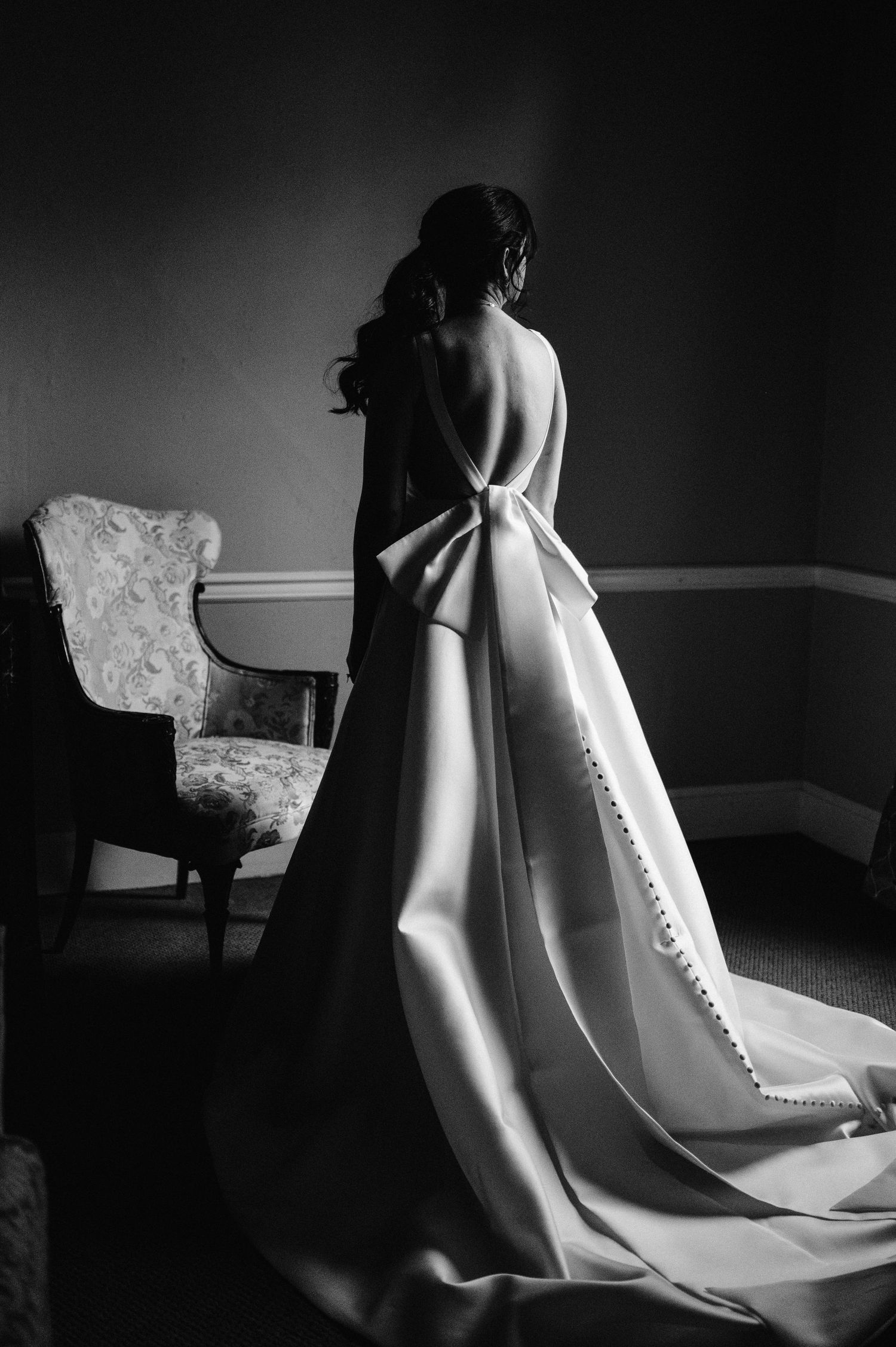 Dramatic black and white photo showing the back of an elegant wedding dress with button details.