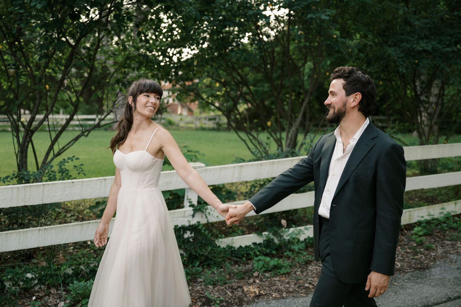 A couple holds hands while walking along a rustic wooden fence on a romantic countryside path.