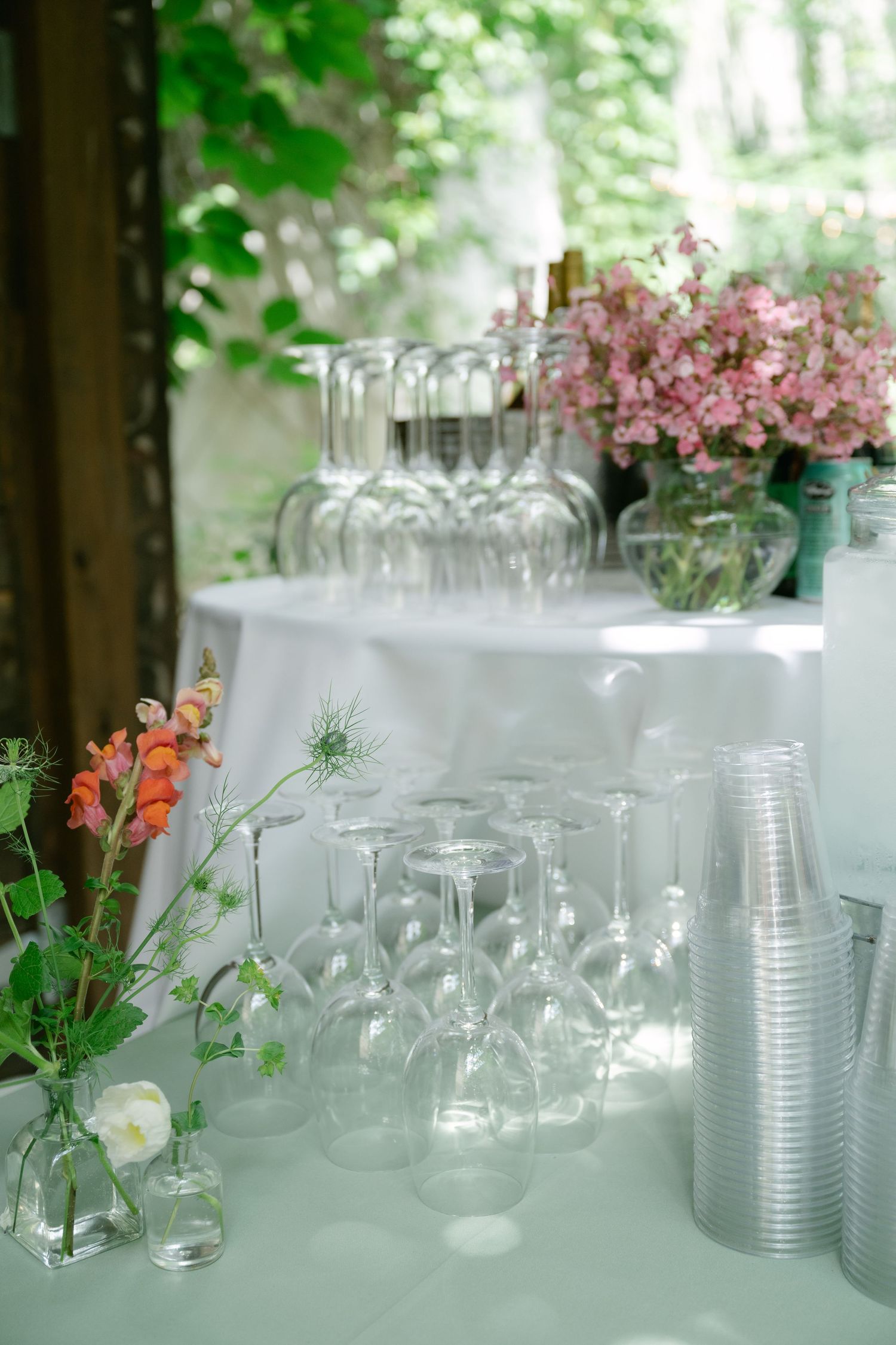 Elegant wedding reception table setup with clear glassware and small floral arrangements against a bright outdoor setting.