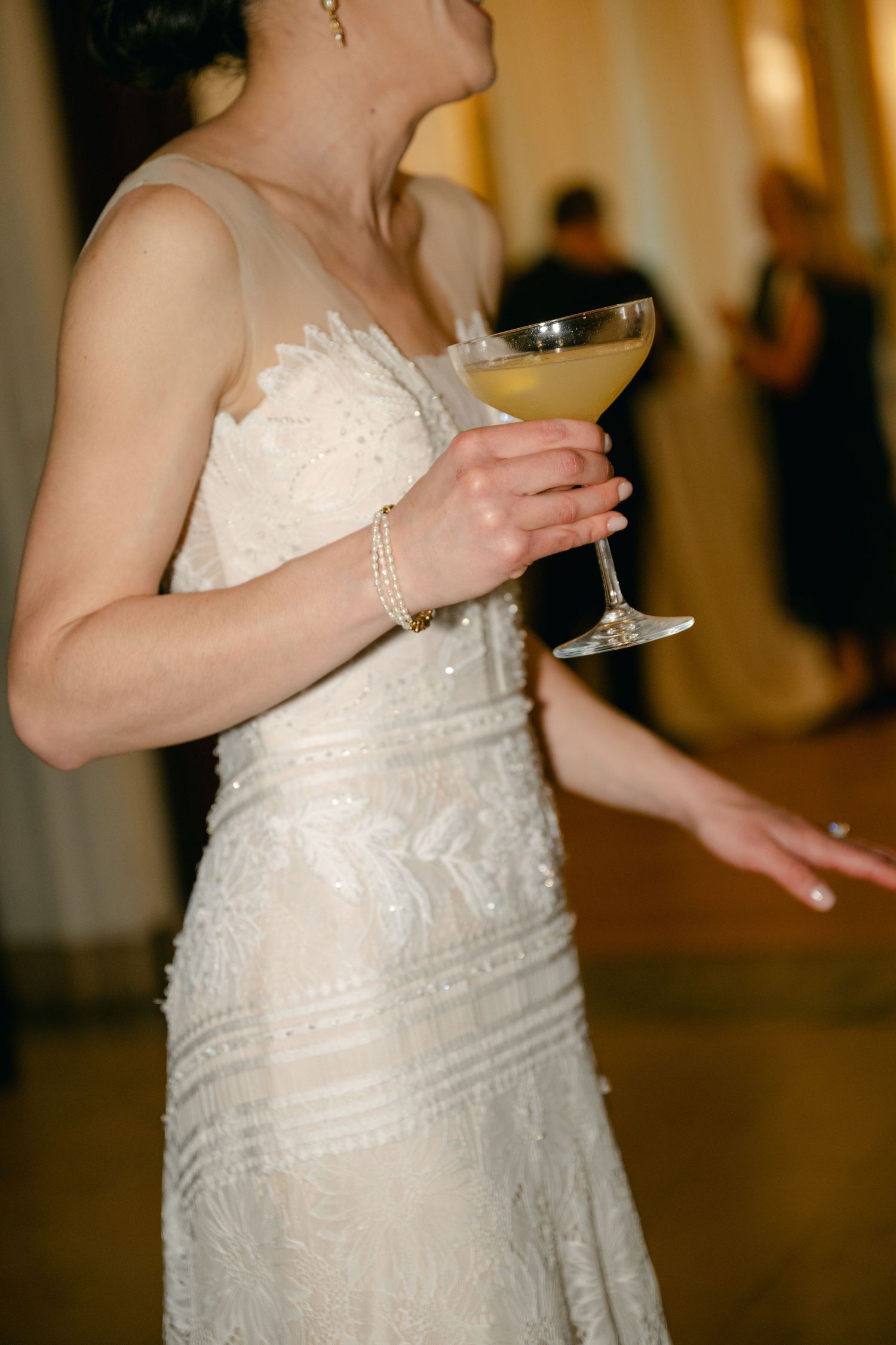 Close up of someone in a lace wedding dress holding a champagne glass during a celebration.