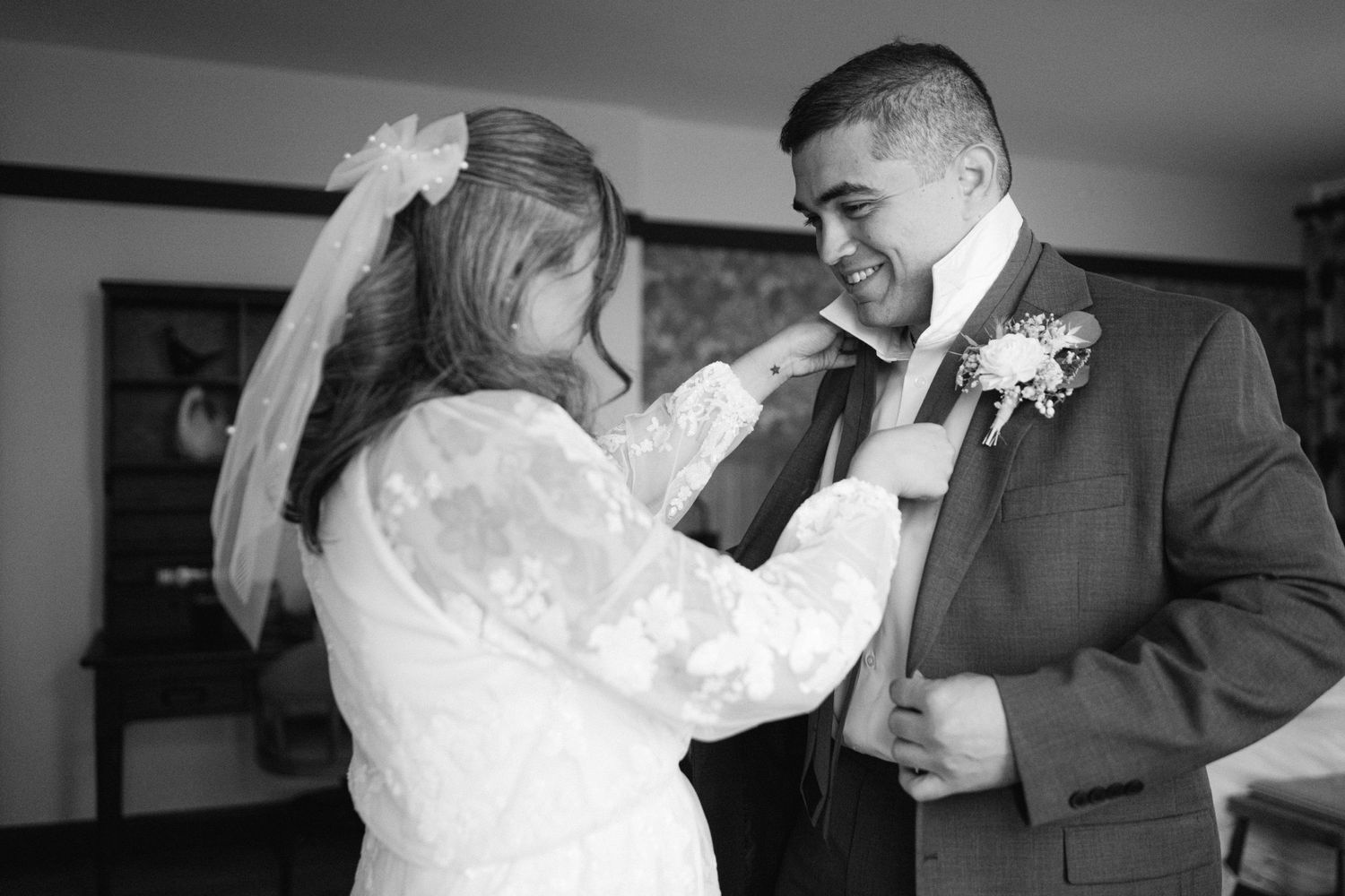 A black and white photo capturing a tender wedding moment between a couple dressed in formal attire.