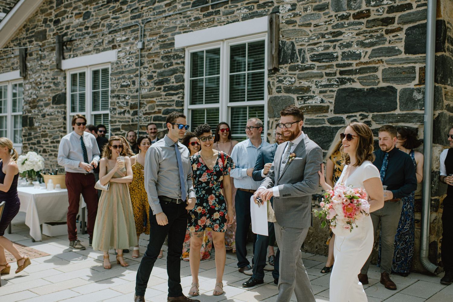 Wedding guests mingling outside stone building during outdoor reception.
