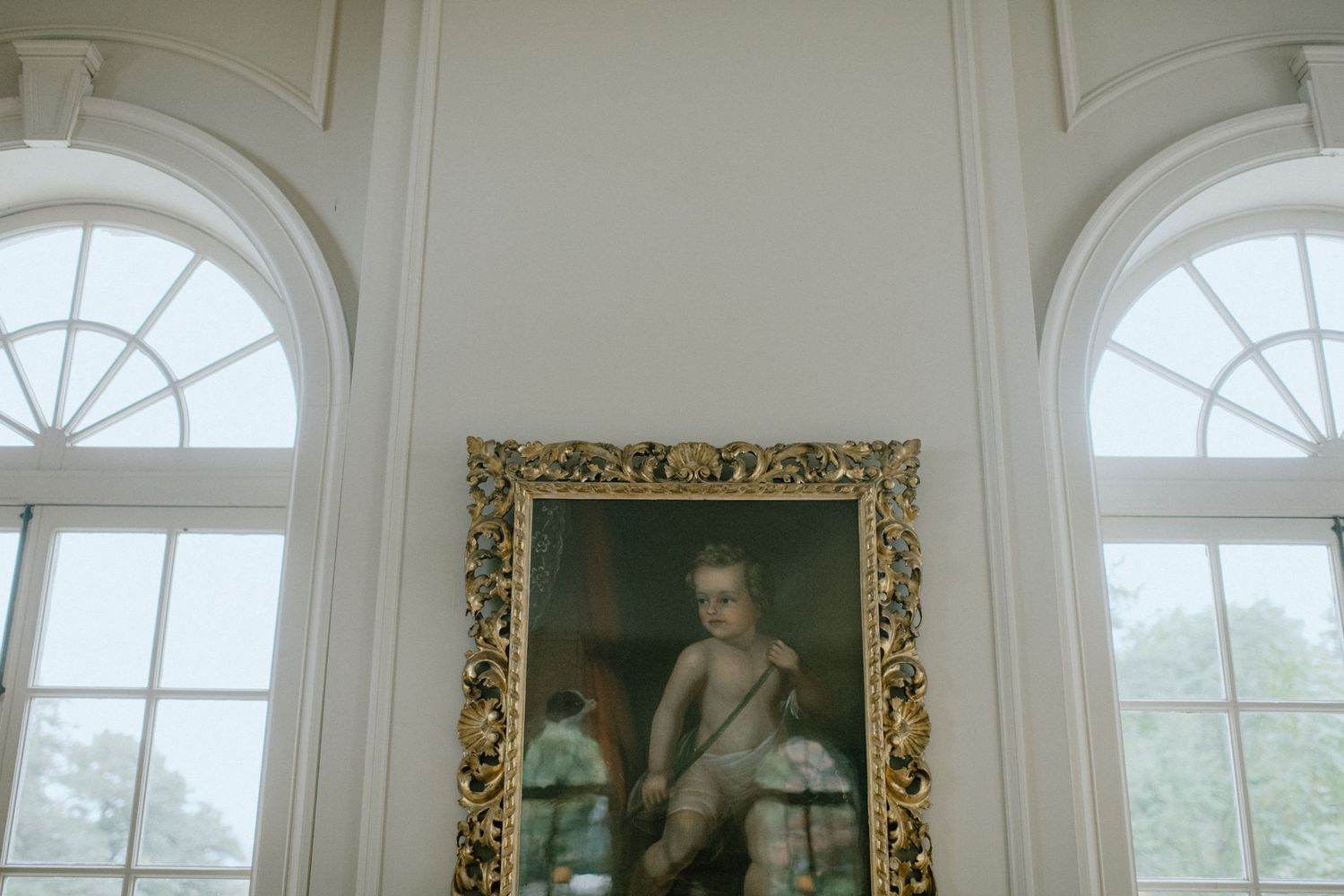 Elegant interior with arched windows and ornate gold-framed portrait.