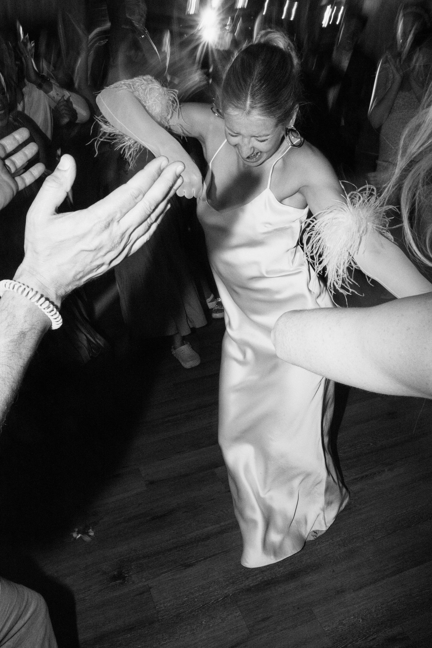 A bride in a silk dress with feather details dances energetically at her reception.