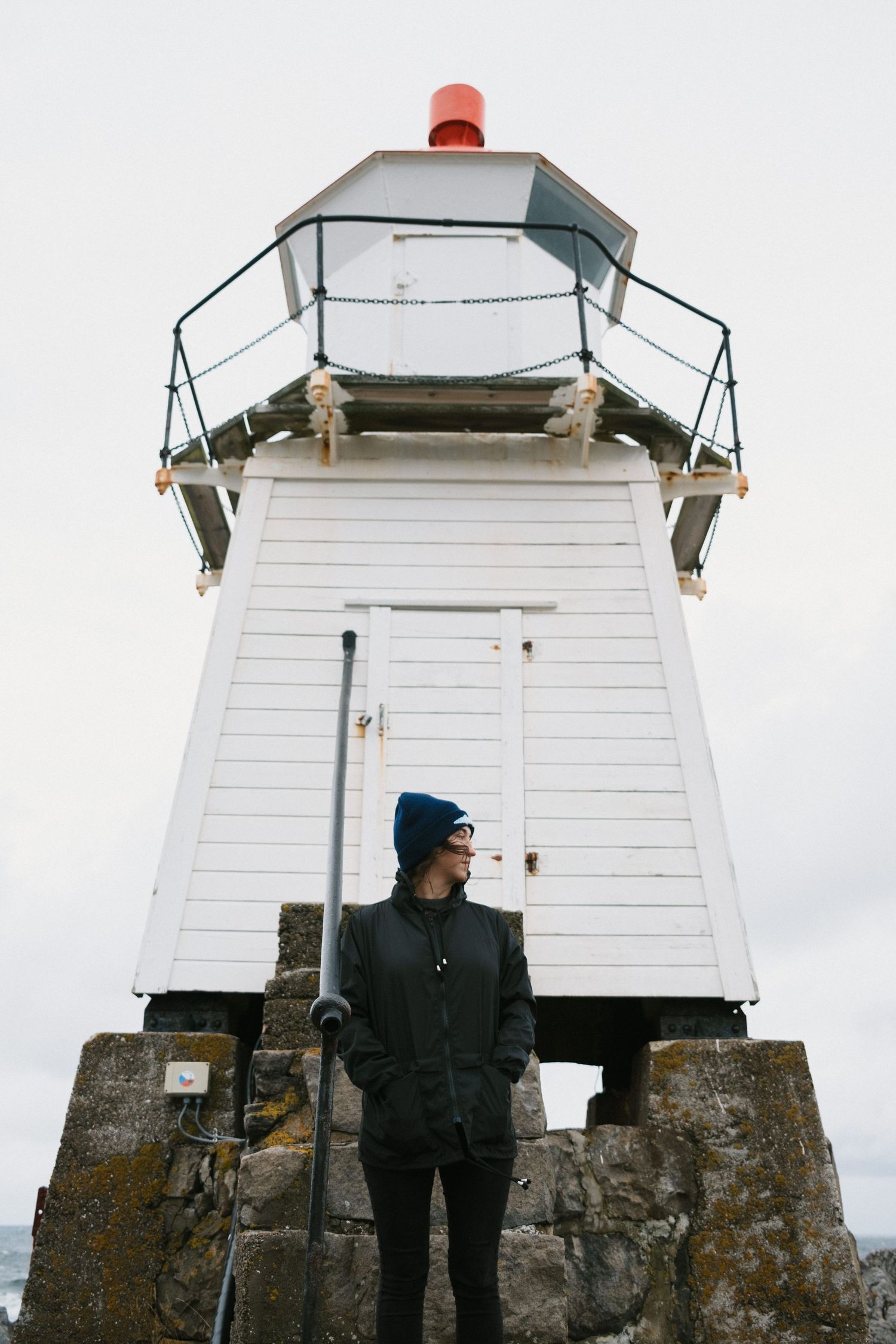 White lighthouse tower stands tall on rugged stone foundation against overcast sky.