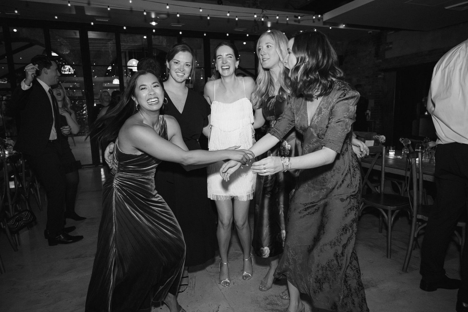A group of party guests dancing together in formal attire at an indoor celebration.