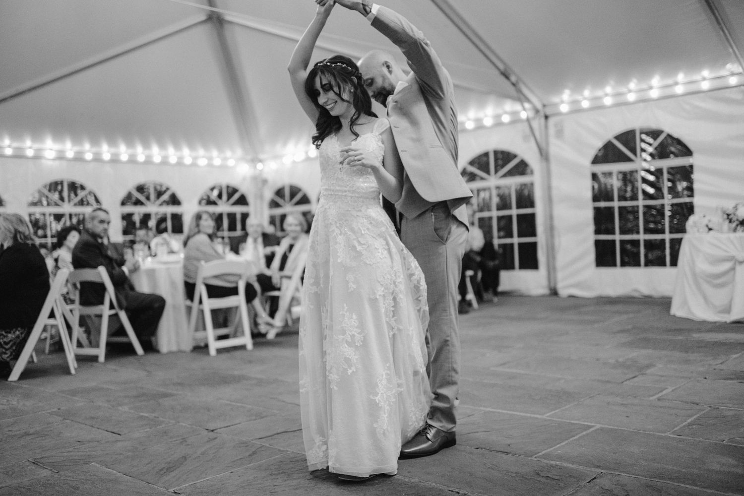 A couple dances together under a white tent with string lights during their wedding reception.