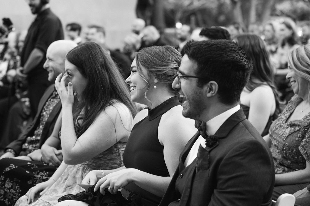A crowd of wedding guests laugh and smile during a joyful reception celebration.