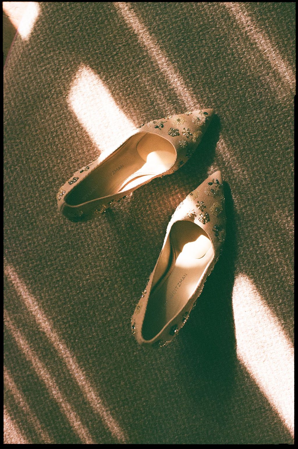 Elegant beige bridal shoes on dark carpet with dramatic diagonal shadows.