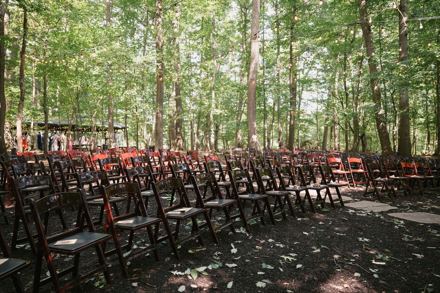 Rows of wooden chairs set up in a wooded outdoor wedding ceremony space.