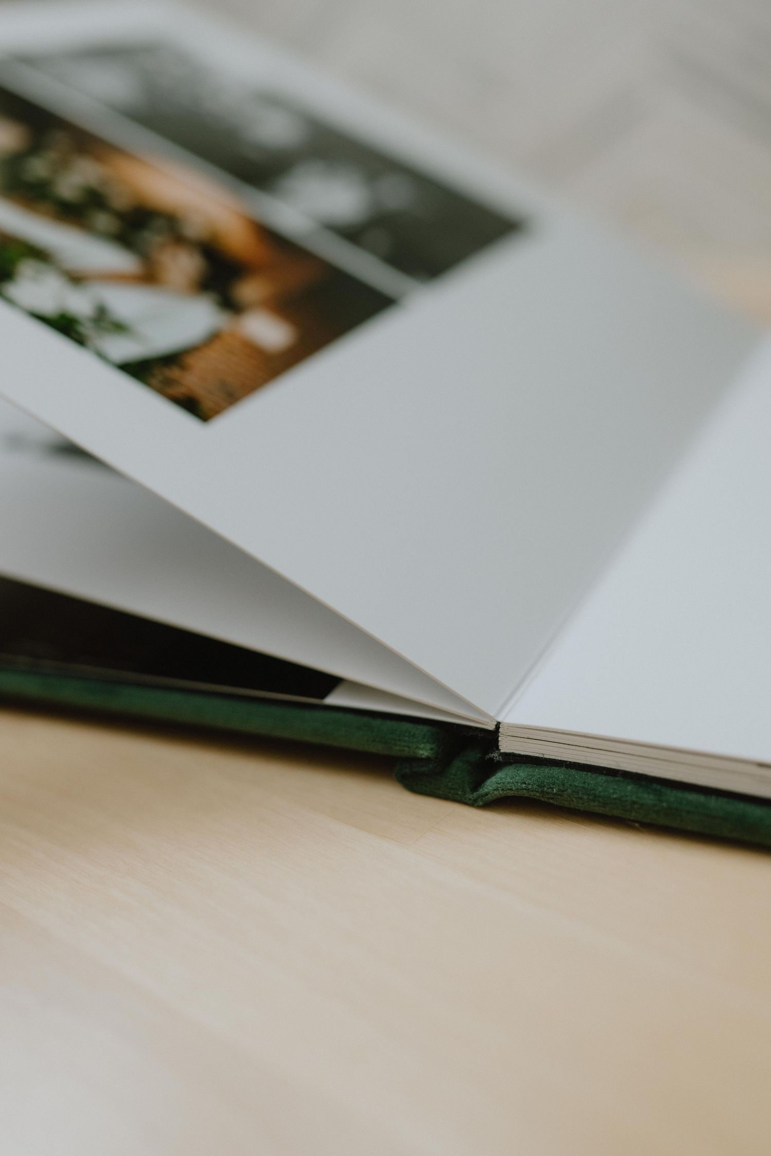 Open green velvet photo album with wedding photos on a wooden surface, showcasing elegant lay-flat binding.