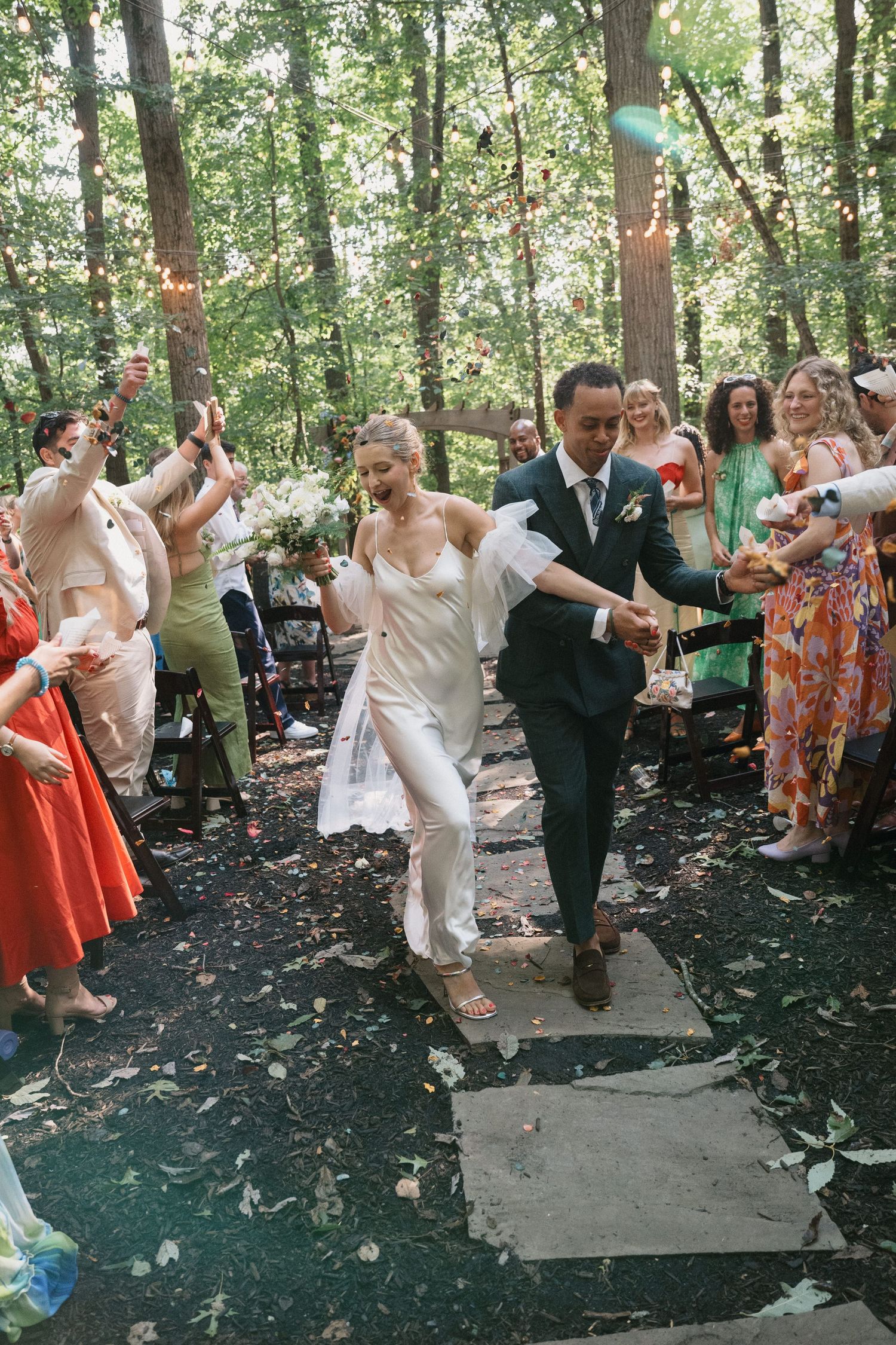 Wedding guests dance and celebrate on an outdoor wooded dance floor.