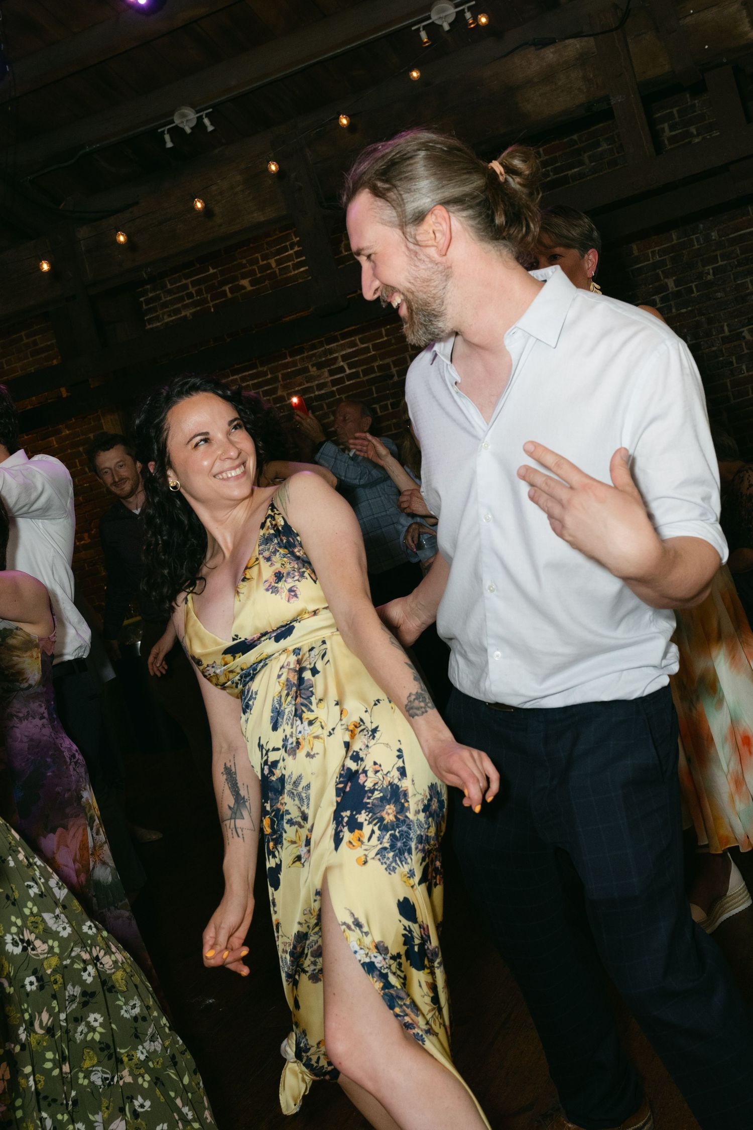 A couple dancing energetically at a wedding reception, with the woman wearing a yellow floral dress.