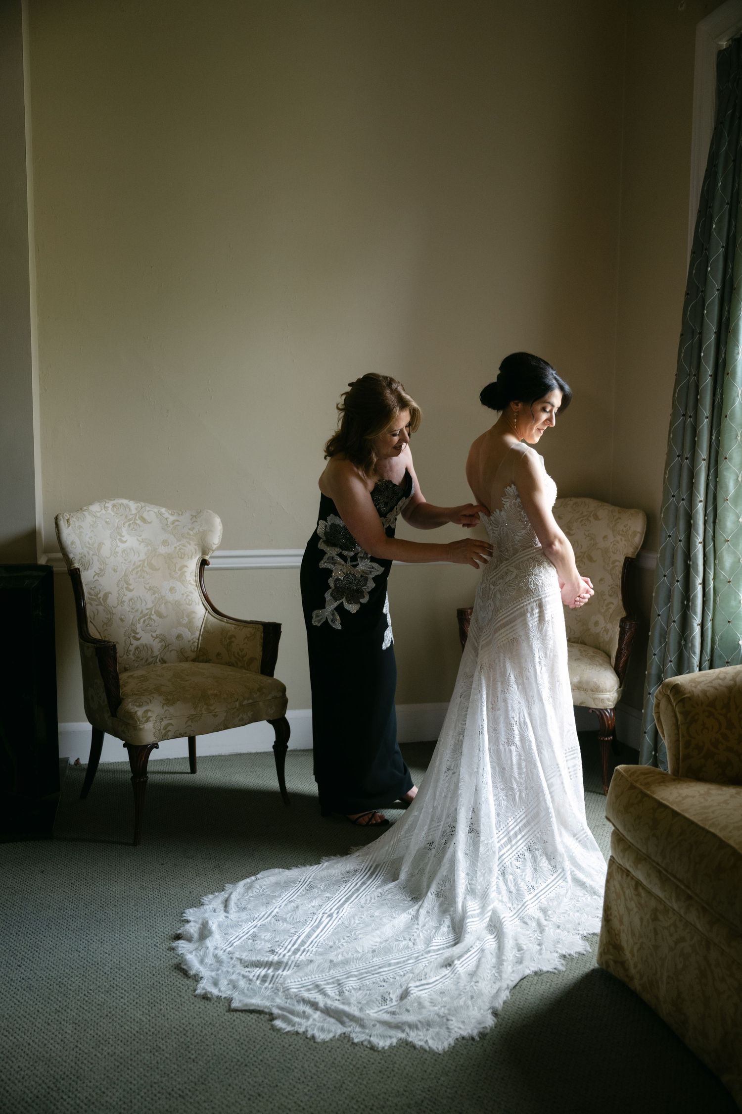 An elegant wedding dress being adjusted in a room with vintage chairs, showing the intricate lace train at a Baltimore engineers club