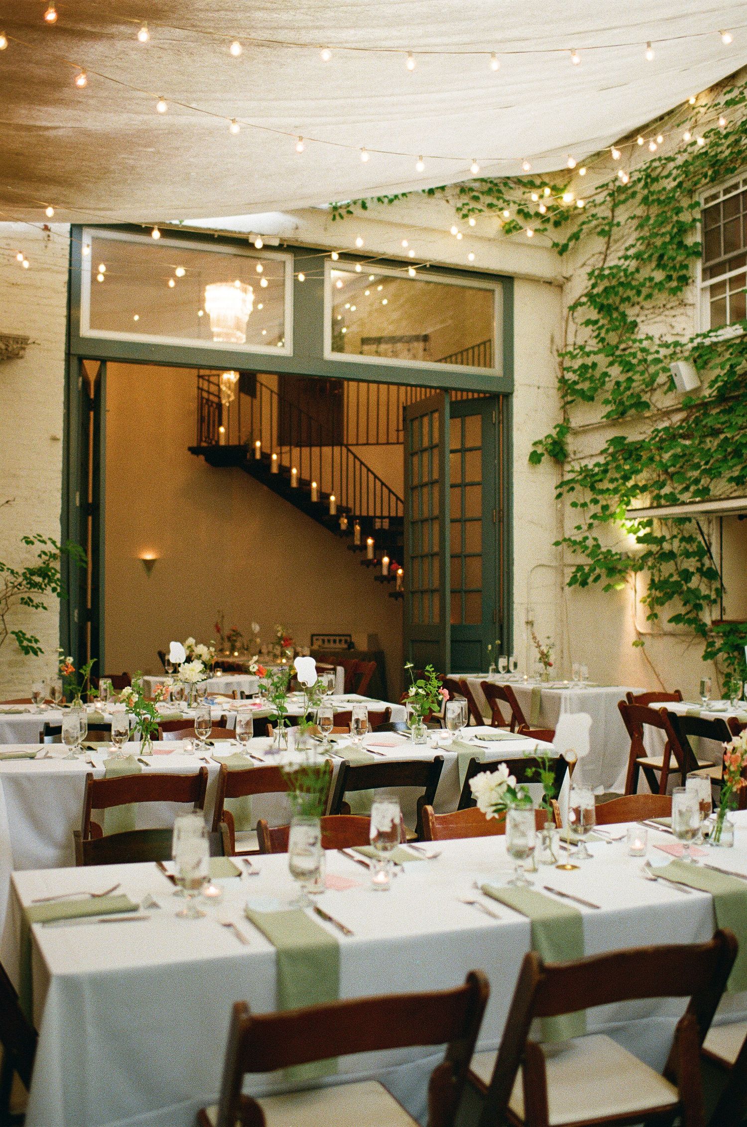 Elegant reception tables set with white linens and string lights in a restaurant dining room with ivy-covered walls.