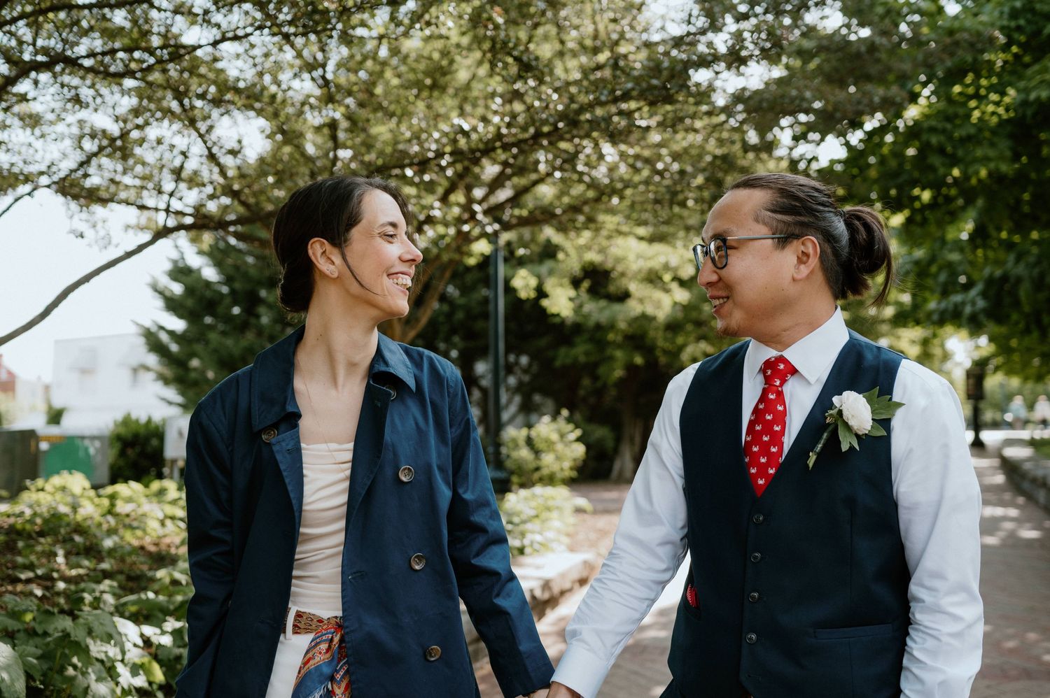 A couple in formal attire walk together in a garden setting.