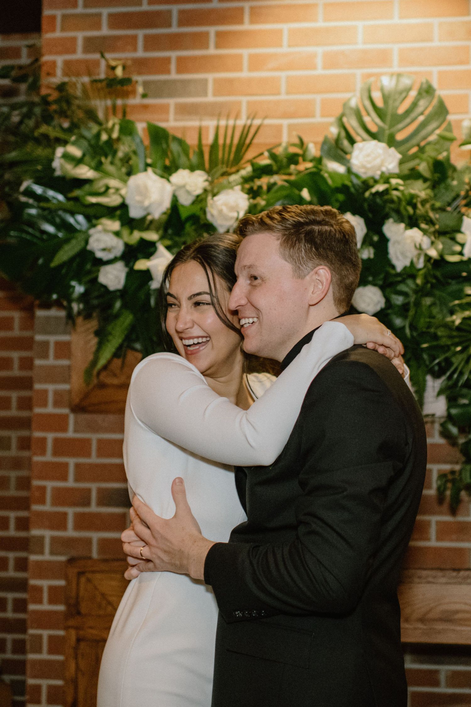 A joyful couple embracing in front of a lush white floral backdrop.