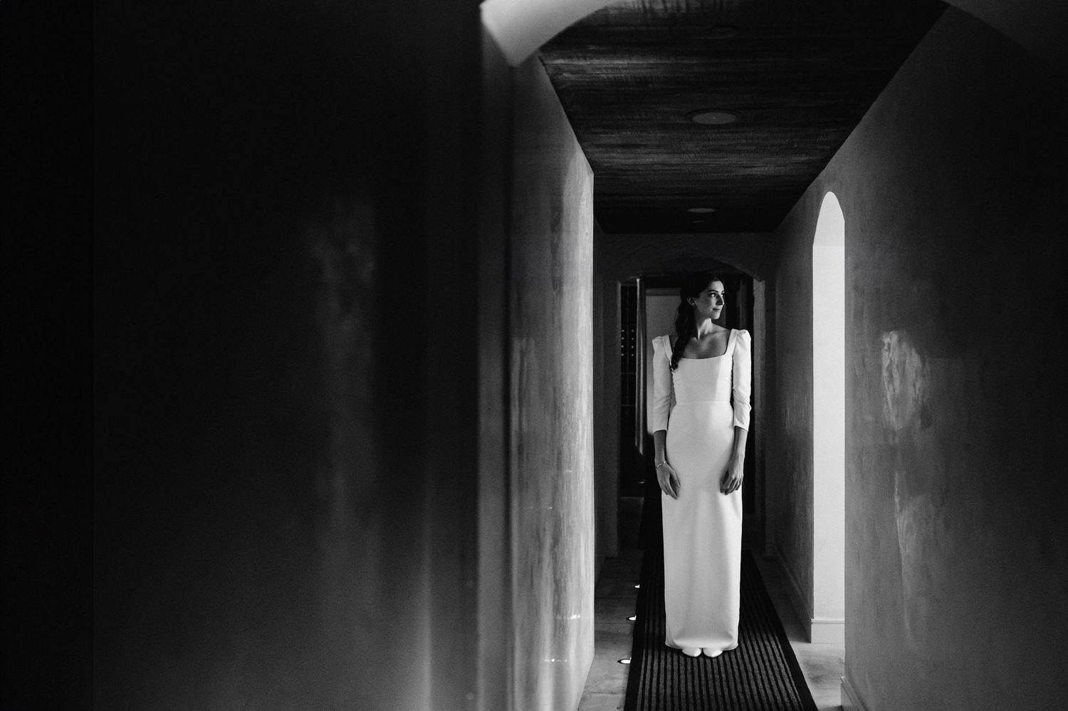 A dramatic black and white photo shows a silhouette in a long dress standing in a dark hallway.