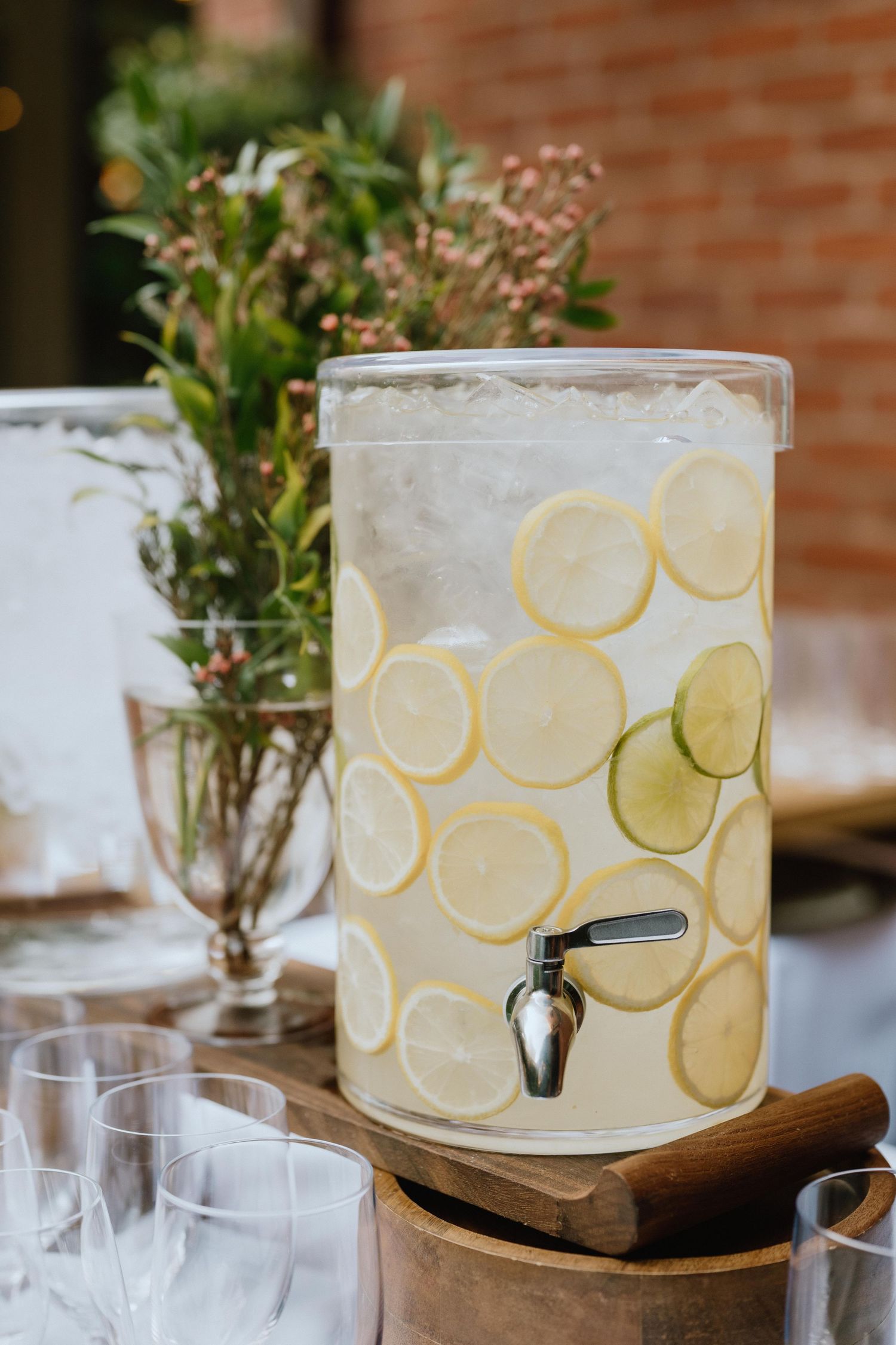 Refreshing citrus-infused water dispenser with lemon and lime slices on wooden stand.