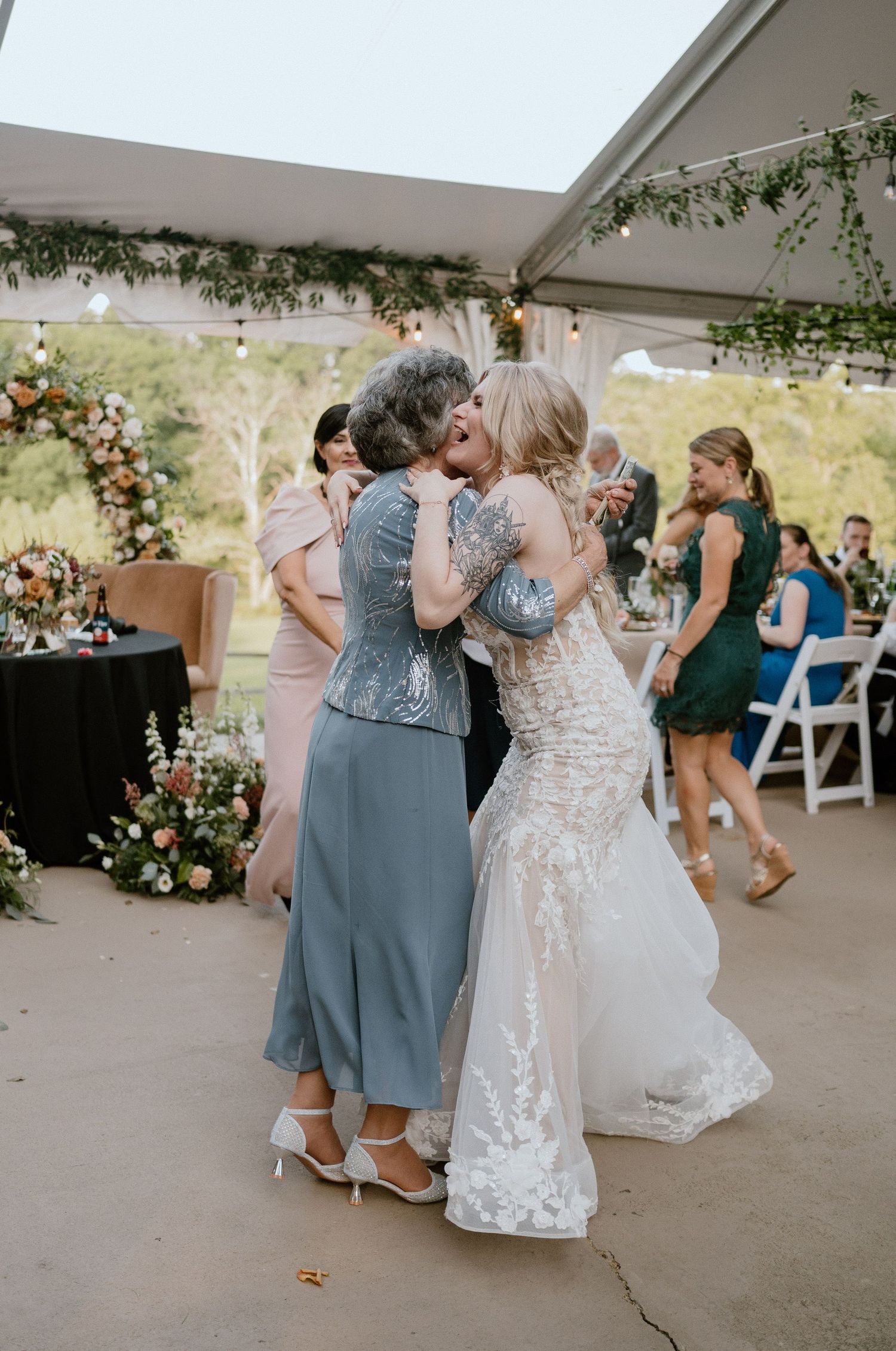 Two people share emotional embrace during wedding reception under decorated tent.