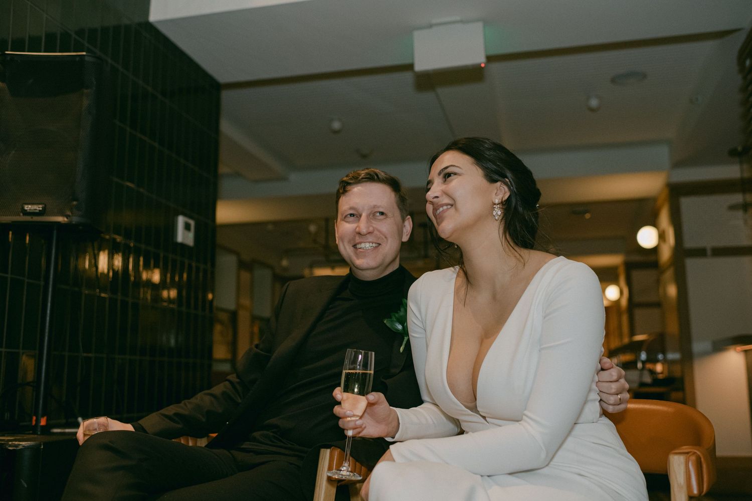 A couple sitting at a bar sharing drinks and laughter during an evening celebration.