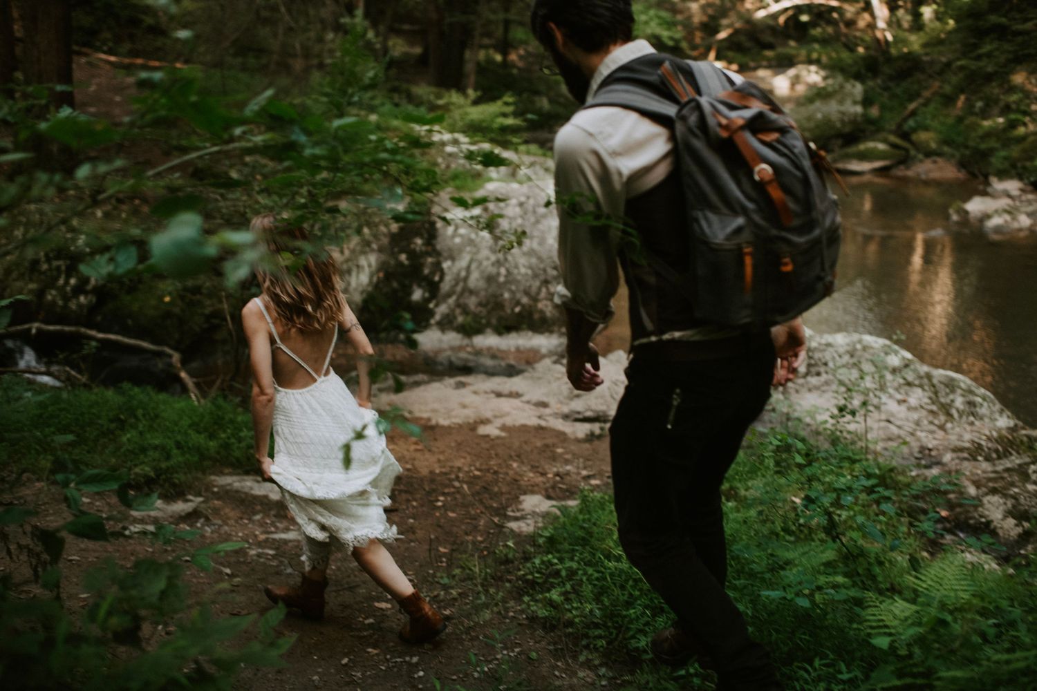 Hikers traverse rocky terrain near a creek in a lush forest setting.