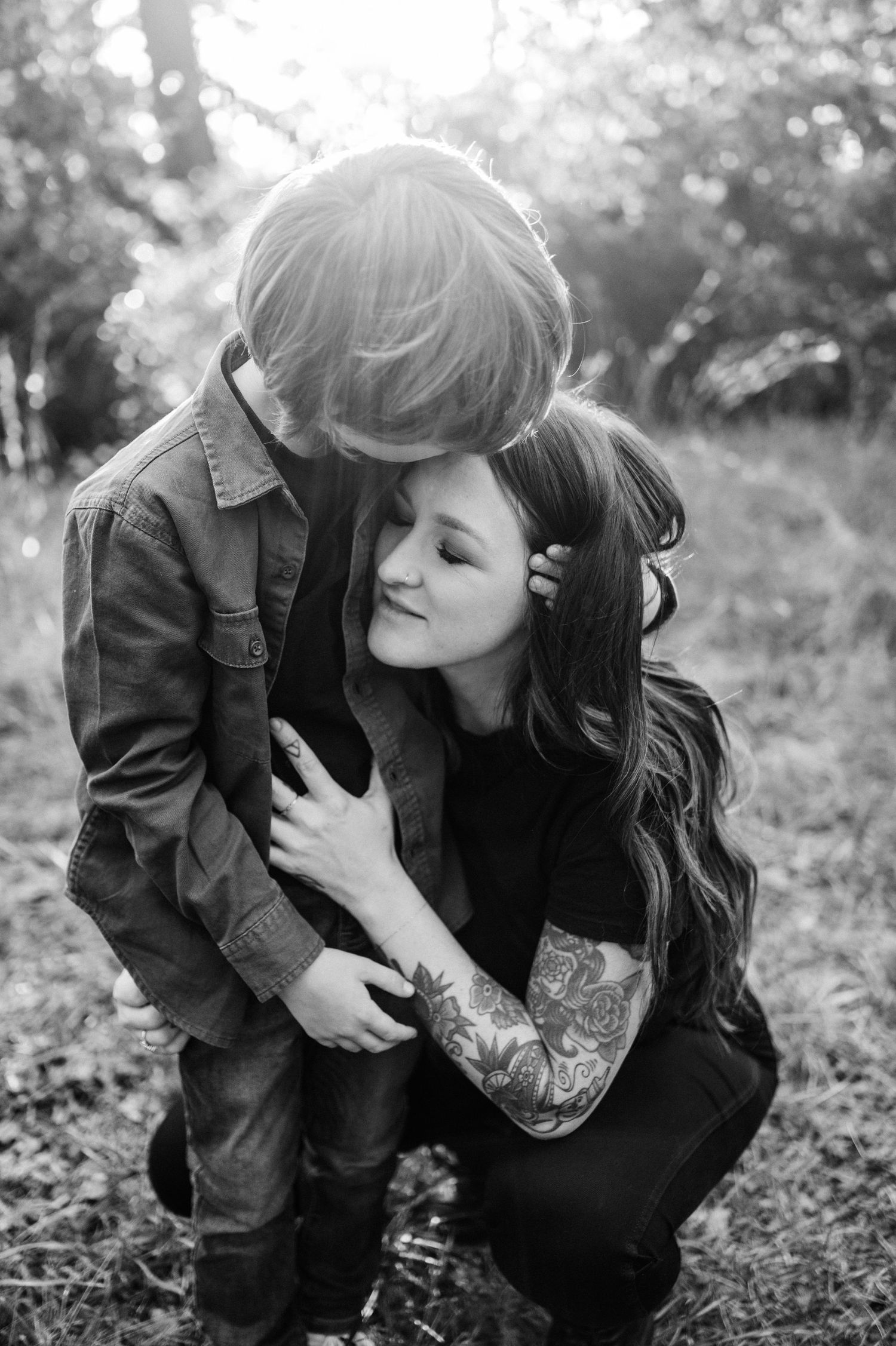 A tender black and white portrait showing an embrace outdoors with visible tattoo art.