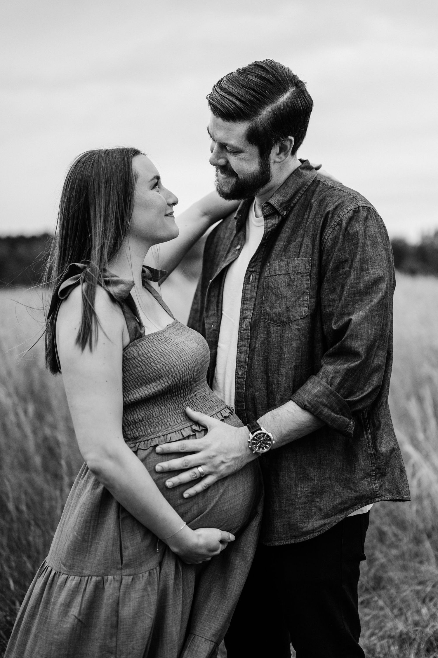 An intimate black and white maternity photo of a couple embracing in a field.