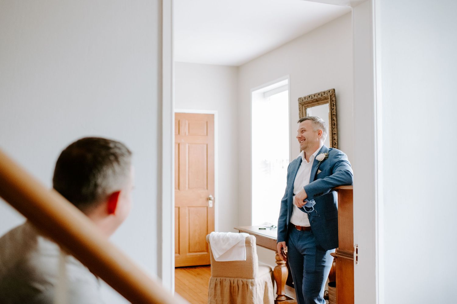 A person in a navy suit stands in a doorway of a bright, minimalist room.