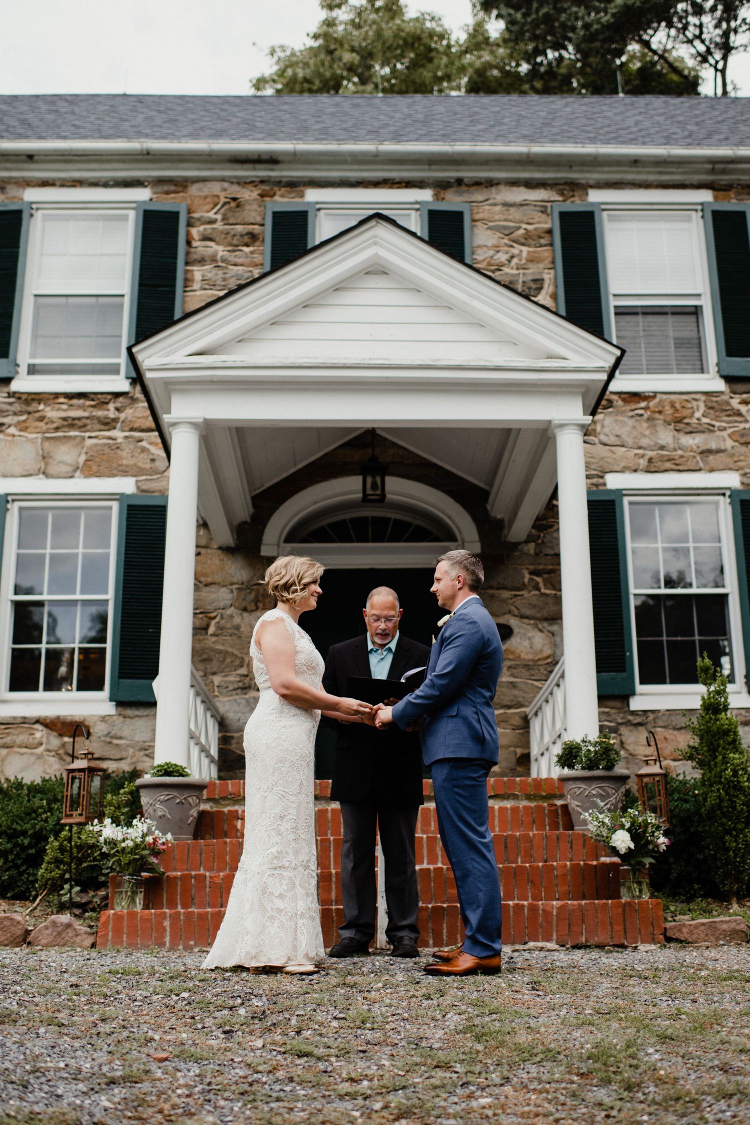 Wedding ceremony under columned entrance of stone colonial house.