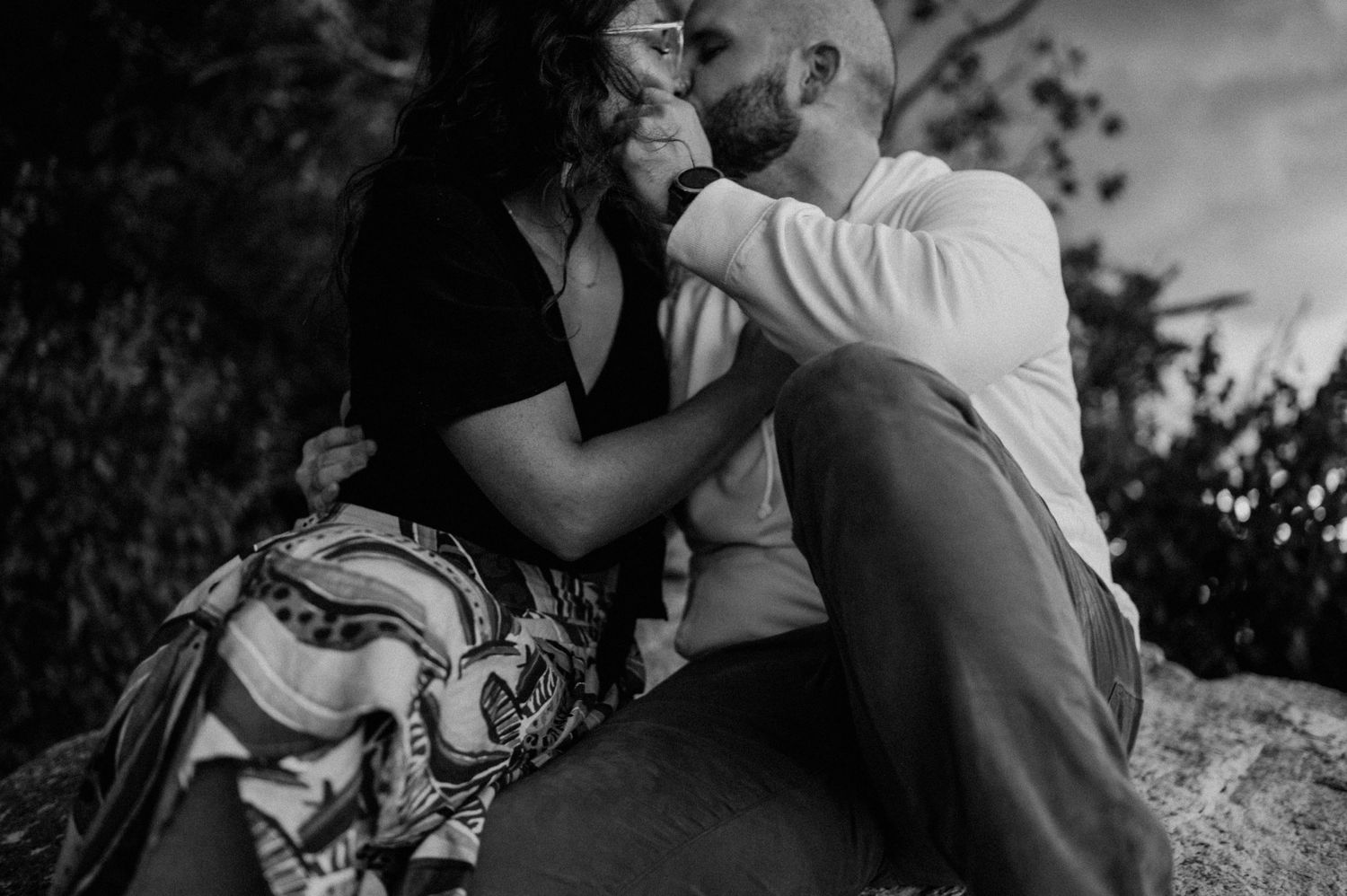 An intimate black and white photo of a couple sharing a tender moment on rocky terrain.