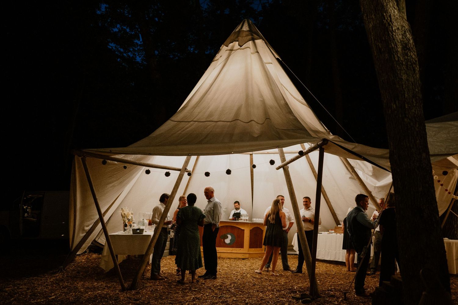 Illuminated white tent at night with silhouettes of guests mingling during an evening outdoor event.