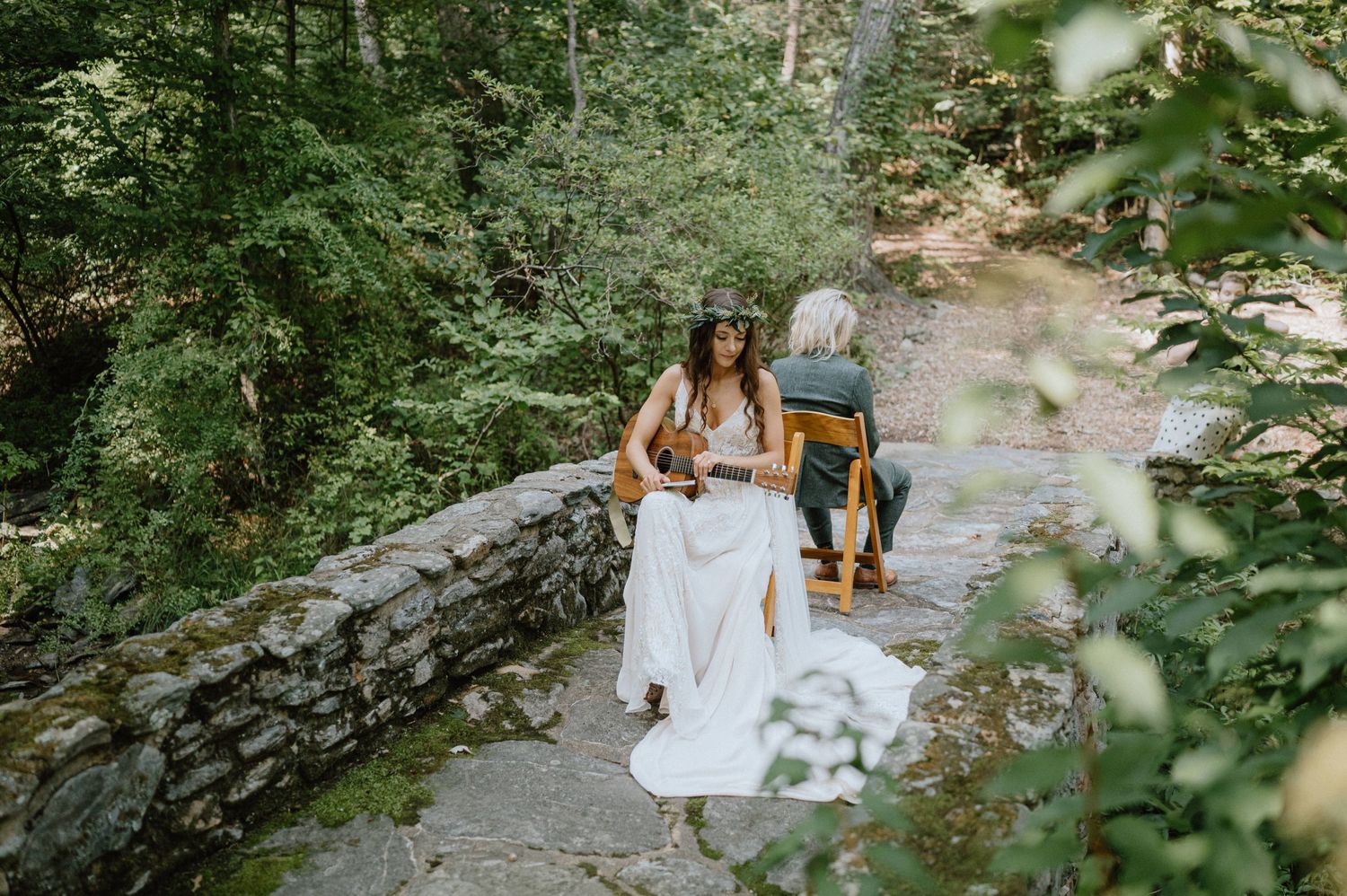 Two people walk along a winding stone path through a lush wooded area on their wedding day.