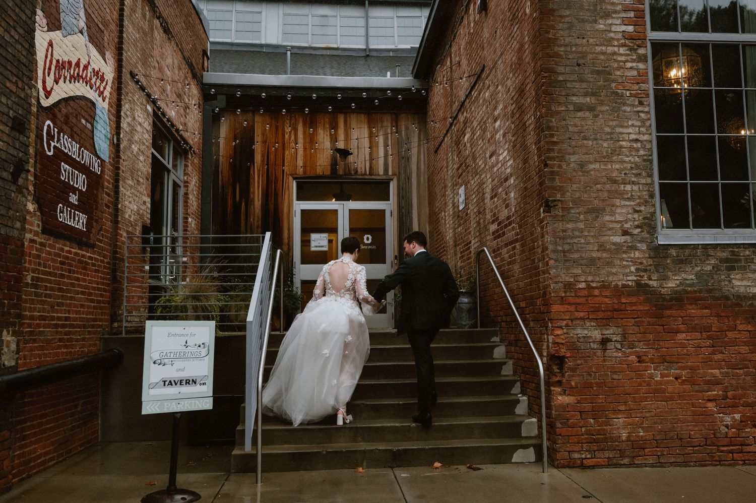 Newlyweds ascend brick stairs to enter historic building entrance.