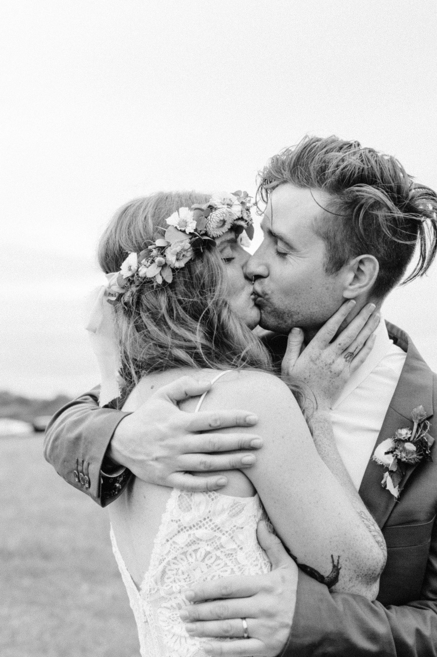 Intimate black and white wedding kiss with flower crown and natural backdrop.