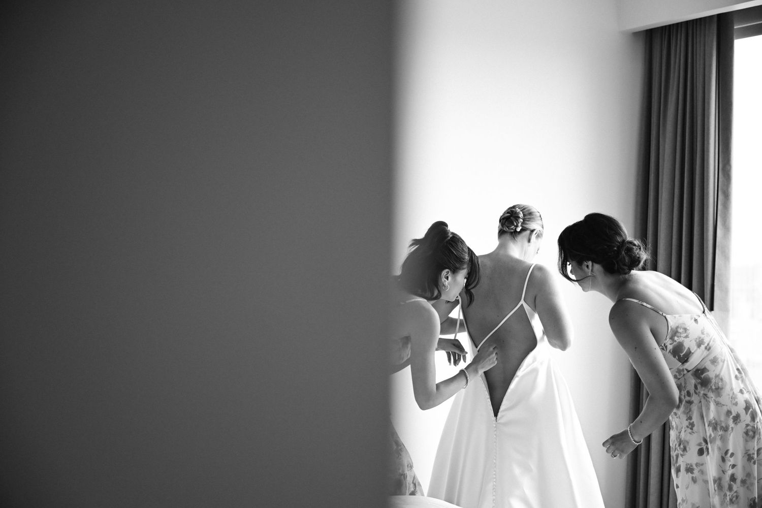 Wedding dress hanging in window light during bridal preparation.