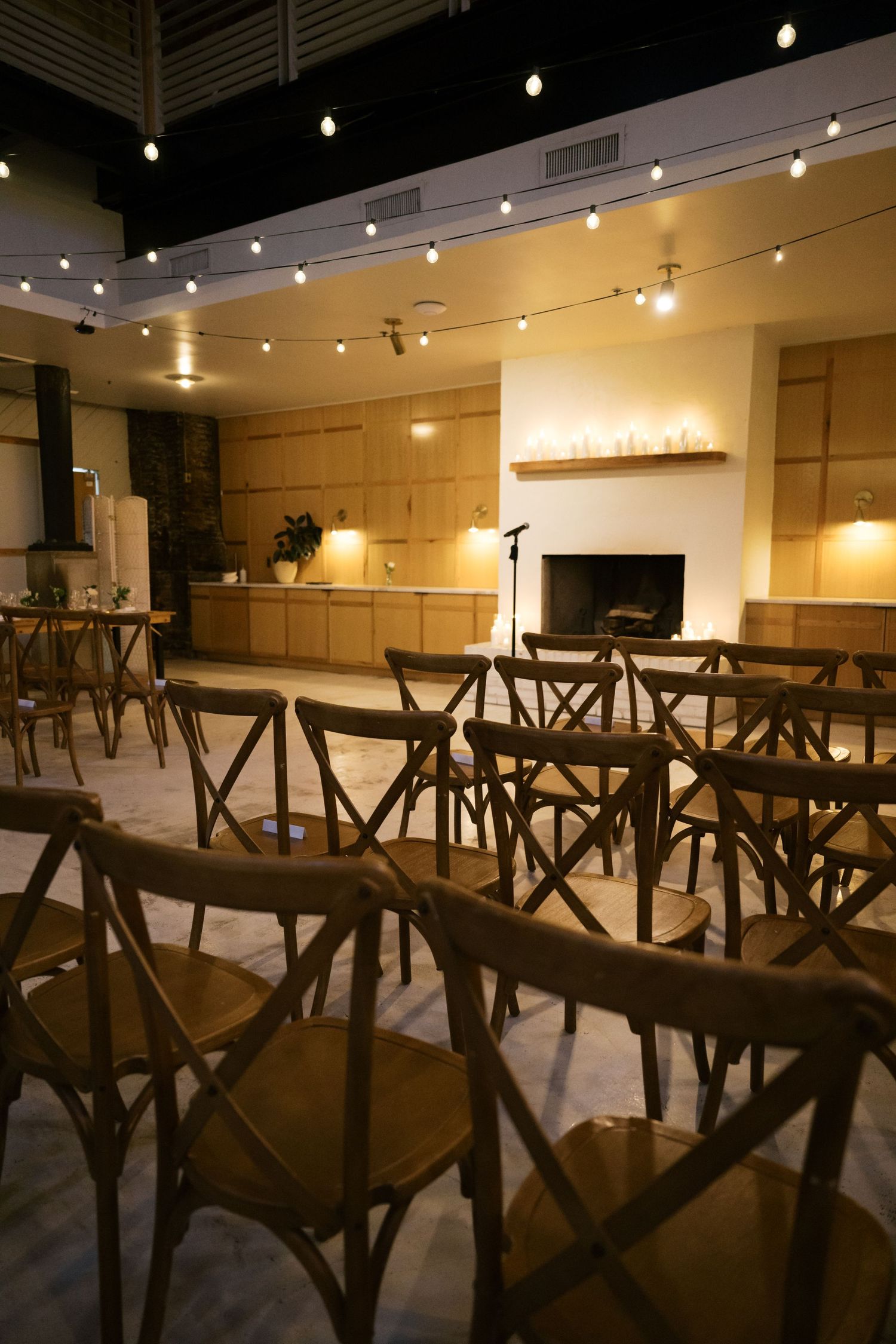 Wedding reception venue with rustic cross-back chairs and romantic string lighting.