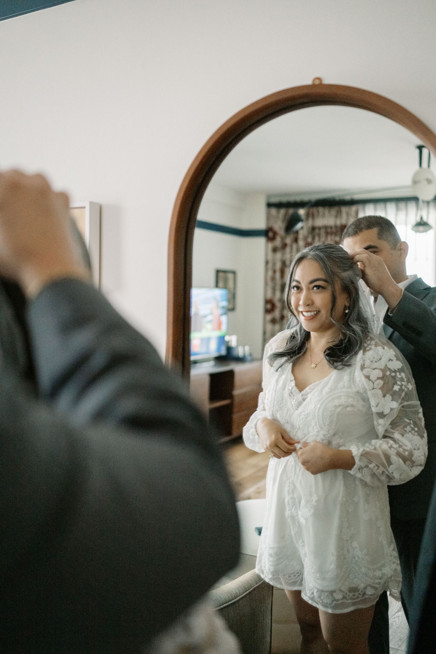 A bride getting ready on her wedding day in a white lace robe as final preparations are made.