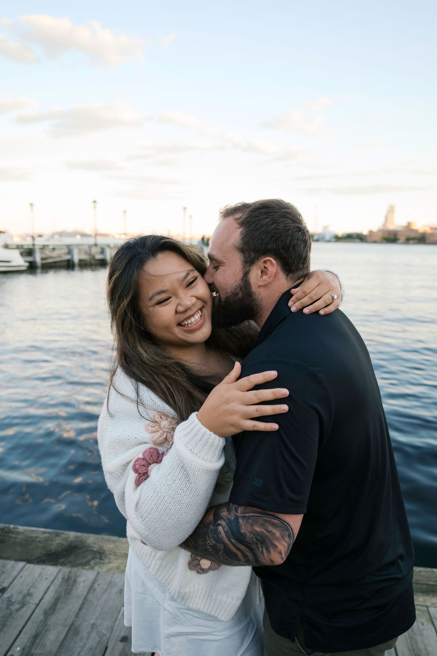 A couple shares a joyful moment embracing on a waterfront dock during golden hour.