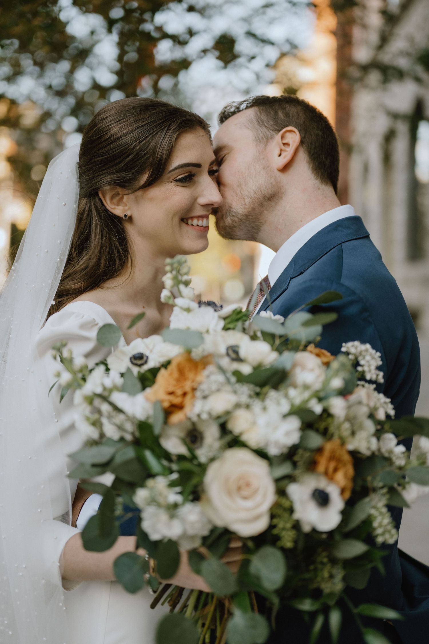 A romantic wedding moment outdoors with a beautiful bouquet of roses, anemones and eucalyptus in soft peach and white tones.