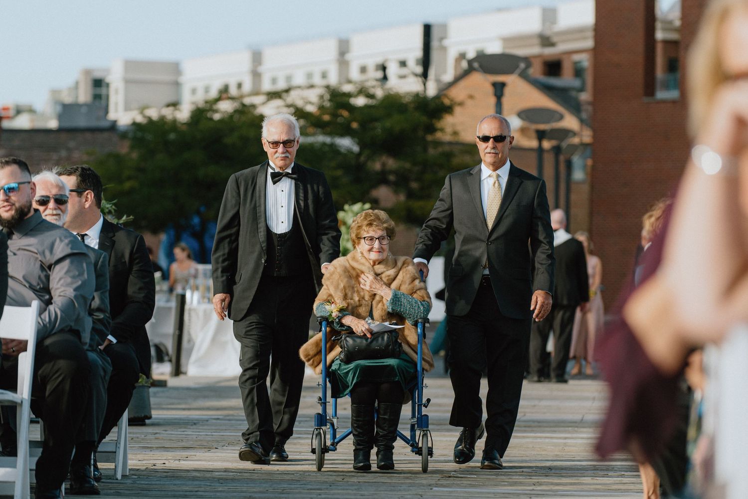Wedding processional walking along waterfront boardwalk on sunny day.