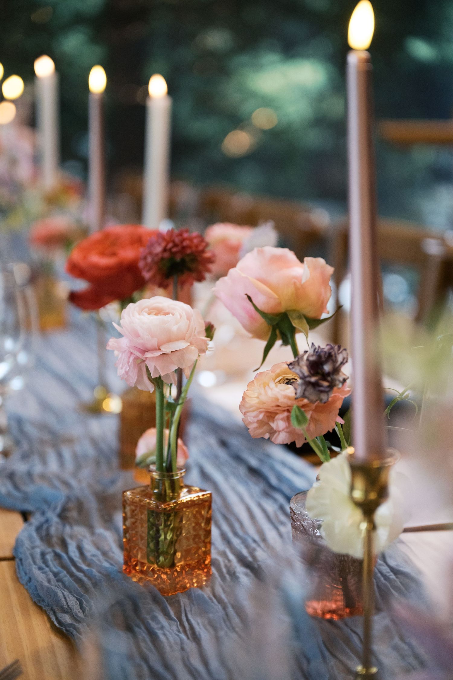 Candlelit table decor with pink and coral roses in amber glass vases on blue silk runner.