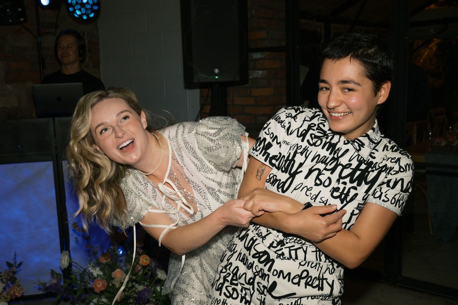 Two people laughing and dancing together at a party with blue lighting in background.