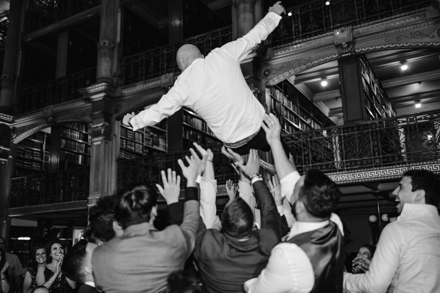 Wedding guests lift a person into the air during a celebratory reception dance moment.