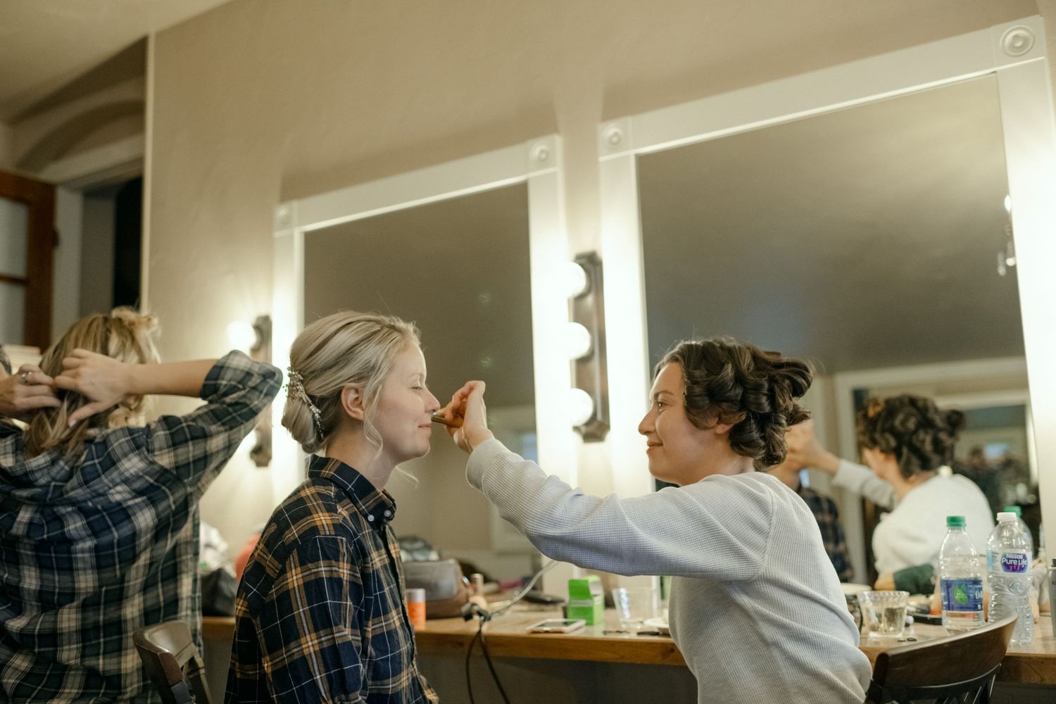 Behind the scenes of wedding preparation with makeup artists working in dressing room.